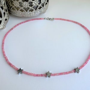 May include: A delicate pink gemstone necklace with three silver star charms. The necklace is made of small, round beads and is perfect for everyday wear.