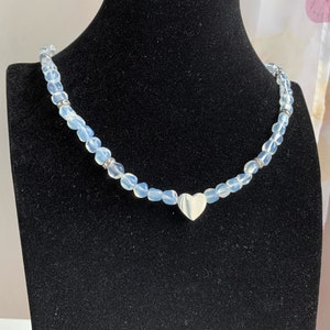 May include: A delicate necklace made with light blue glass beads and a silver heart charm.