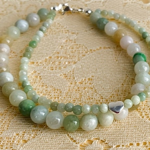 May include: A double-strand jade bracelet with a silver heart charm. The bracelet features green and white jade beads of varying sizes.