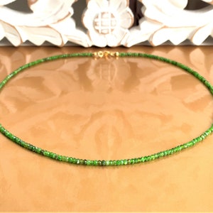May include: A fine necklace composed of small, bright green beads. The necklace is fastened with a gold-coloured clasp. The beads are a deep, emerald green, creating a simple yet elegant piece of jewellery.