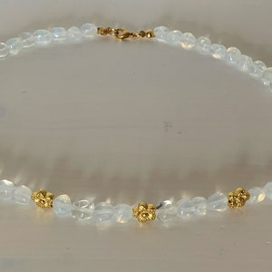 May include: A white opal beaded necklace with gold flower accents.