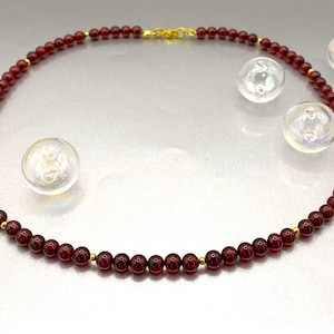 Puede incluir: Un collar de cuentas de granate rojo con un cierre de oro. El collar está hecho de pequeñas cuentas redondas y tiene aproximadamente 45 cm de largo.