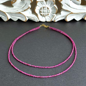 Könnte beinhalten: Eine mehrreihige Halskette mit kleinen, facettierten rosa Edelsteinen. Die Halskette hat einen goldfarbenen Verschluss und wird vor einem dunklen Hintergrund präsentiert. Die Edelsteine haben einen leuchtenden Rosaton.