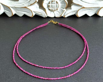 Op de afbeelding: Een gelaagde ketting met kleine, gefacetteerde roze edelstenen. De ketting heeft een goudkleurige sluiting en wordt gepresenteerd tegen een donkere achtergrond. De edelstenen hebben een levendige roze tint.