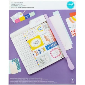 May include: A white and lavender guillotine cutter with a grid base, designed for paper crafts. The cutter features a lavender handle and blade, with the text "HEY Sugar" visible on the cutting surface. The cutter measures 12 x 12 inches.