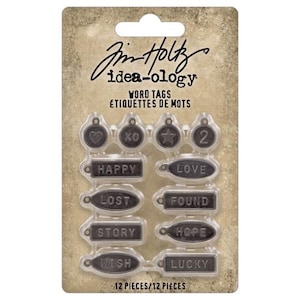 May include: A package of 12 metal word tags with a variety of words and designs. The tags are silver and black and have a distressed look. The words on the tags include "Happy", "Love", "Lost", "Found", "Story", "Hope", "Wish", and "Lucky".