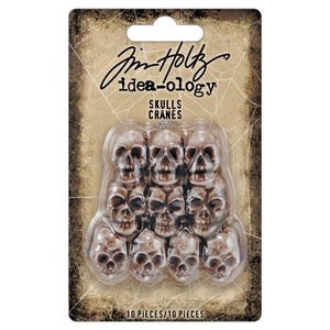 May include: A package of ten small, brown skull-shaped embellishments. The package has the text "Jim Holtz idea-ology" and "SKULLS CRANES" printed on it. The package also has the text "10 PIECES/10 PIECES" printed on it.