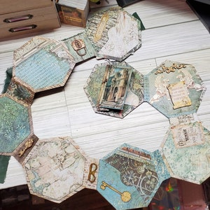 Puede incluir: Un &aacute;lbum hexagonal con p&aacute;ginas de papel con diferentes patrones. Cada p&aacute;gina presenta un dise&ntilde;o diferente, incluyendo un castillo, un p&aacute;jaro y una llave. El &aacute;lbum est&aacute; abierto y colocado plano sobre una superficie de madera.
