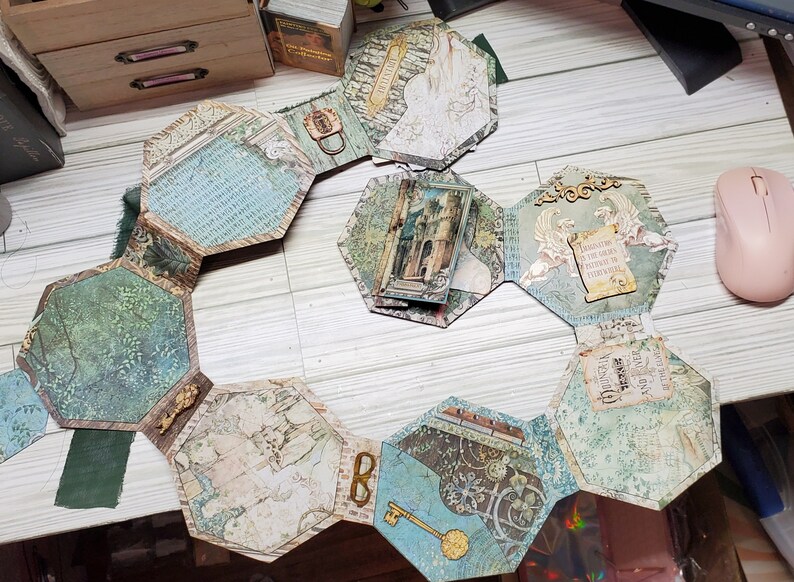 Puede incluir: Un &aacute;lbum hexagonal con p&aacute;ginas de papel con diferentes patrones. Cada p&aacute;gina presenta un dise&ntilde;o diferente, incluyendo un castillo, un p&aacute;jaro y una llave. El &aacute;lbum est&aacute; abierto y colocado plano sobre una superficie de madera.