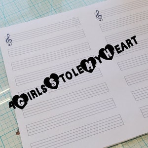 May include: A white sheet of paper with two sets of music staff lines. The text "Girls stole my heart" is printed in black across the top of the paper.