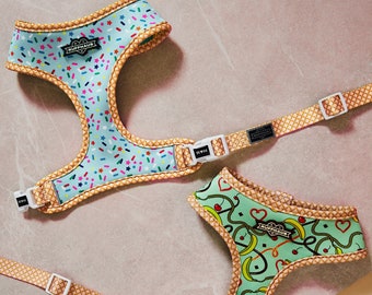 Può includere: Due pettorine per cani con cinturini regolabili e un motivo a forma di waffle. Le pettorine sono realizzate in un materiale morbido e confortevole e presentano un design divertente e colorato. La pettorina superiore ha uno sfondo blu con spolverate colorate e il testo "Ruffhaus" in un cuore bianco. La pettorina inferiore ha uno sfondo verde con banane, ciliegie e cuori. Il testo "Ruffhaus" è in un cuore bianco sulla pettorina inferiore.