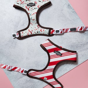 May include: Two dog harnesses with adjustable straps and buckles. One harness is red and white striped with a brown trim. The other harness is green and white with a brown trim and a red and white candy cane pattern. Both harnesses have the brand name "Ruffhaus" printed on them.