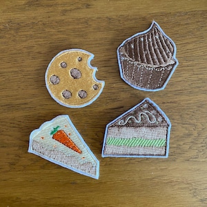 May include: Four embroidered food patches. Includes a chocolate chip cookie with a bite taken out, a chocolate cupcake, a slice of carrot cake, and a slice of chocolate cake with green filling.