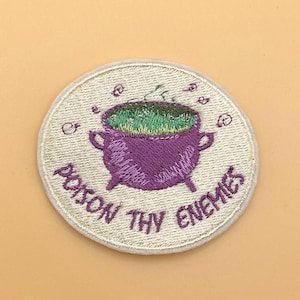 May include: A circular embroidered patch featuring a purple cauldron with green bubbling liquid. The text POISON THY ENEMIES is stitched in purple thread below the cauldron, with small purple swirls surrounding the top of the pot.