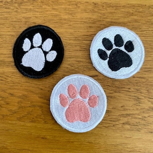 May include: Three embroidered paw print patches. One patch is black with a white paw print, one is white with a black paw print, and one is white with a pink paw print.