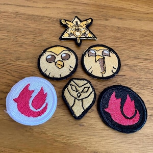 May include: Six embroidered iron-on patches featuring a variety of designs, including a winged owl, a flame, and a geometric symbol. The patches are all different colours and sizes.
