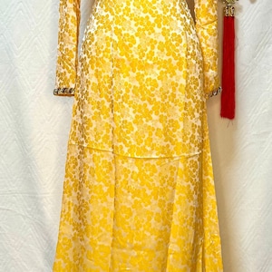May include: A yellow long-sleeved dress with a white floral pattern. The dress has a round neckline and a beaded trim around the neckline and sleeves.