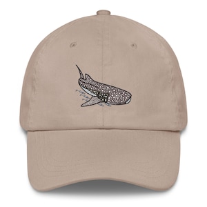 Könnte beinhalten: Eine beige Baseballkappe mit einem gestickten Bild eines Walhais, der mit einem Fischschwarm schwimmt.