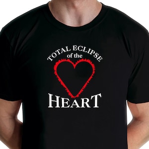 Può includere: Maglietta nera con una grafica bianca che dice "Total Eclipse of the Heart" con un cuore rosso al centro.