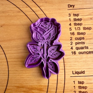 May include: Purple plastic cookie cutter shaped like a rose with leaves.