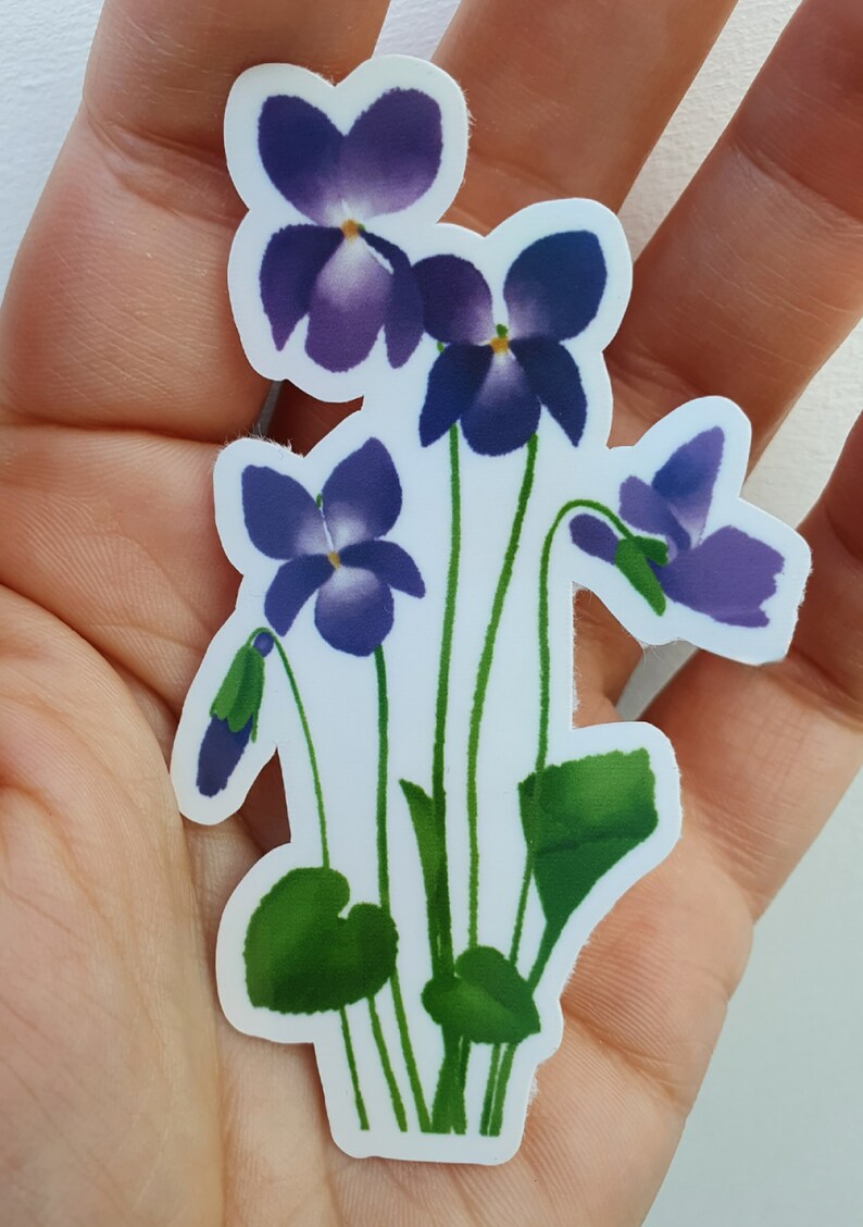 May include: A sticker featuring a cluster of purple and green flowers. The flowers are stylized and have a watercolor-like appearance. The sticker is on a white background.