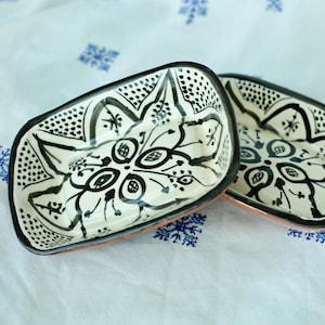 May include: Two white ceramic rectangular dishes with black and white floral designs. The dishes have a raised rim and are stacked on top of each other.