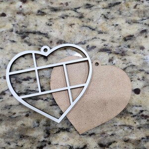 May include: Two unfinished wooden heart-shaped ornaments. One heart has a grid pattern cut out of it. The other heart is solid.