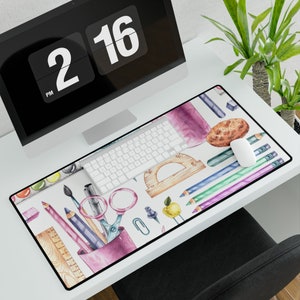 Peut inclure: Un tapis de bureau blanc avec un motif aquarelle coloré de fournitures scolaires, y compris des crayons, des ciseaux, une règle, une palette de peinture et une pomme. Le motif comprend également un rapporteur, un compas et un biscuit.