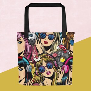 以下が含まれることがあります： サングラス、ヘッドフォン、カメラを身に着けた女性のポップアートデザインのトートバッグ。バッグには黒いハンドルと、漫画にインスパイアされたカラフルなプリントが施されています。女性はピンク、ブロンド、黒など、さまざまな髪の色をしています。