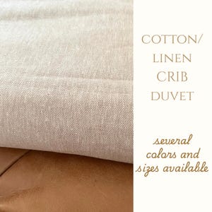 May include: Close-up of a beige cotton/linen crib duvet. The fabric has a textured appearance. The image also includes text that reads "COTTON/LINEN CRIB DUVET" and "several colors and sizes available".