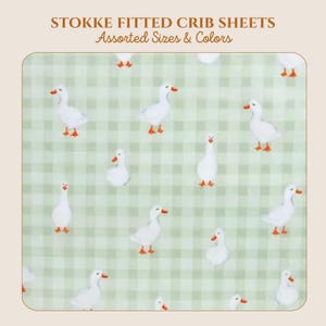 May include: Stokke fitted crib sheets with assorted sizes and colors. The fabric features a light green and white gingham check pattern decorated with a repeating print of white geese with orange beaks and feet scattered across the surface.