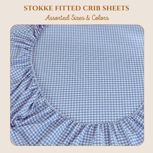 May include: A fitted crib sheet with a blue and white gingham pattern. The sheet has elastic edges and is designed to fit a Stokke crib. The text "STOKKE FITTED CRIB SHEETS Assorted Sizes & Colors" is at the top.