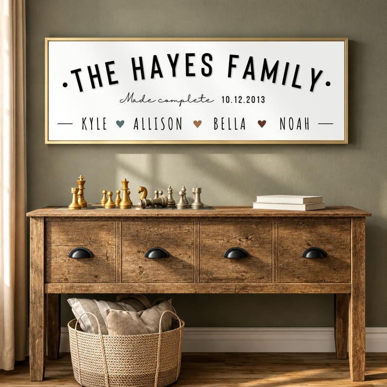 May include: A rectangular wall sign with a gold frame and white background featuring the black text THE HAYES FAMILY, the script text Made complete, the date 10.12.2013, and the names KYLE, ALLISON, BELLA, and NOAH separated by small colored hearts.