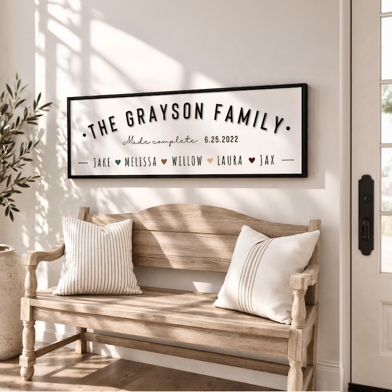 May include: A rectangular wall sign with a black frame and white background featuring the text THE GRAYSON FAMILY, Made complete 6.25.2022, and a list of names including Jake, Melissa, Willow, Laura, and Jax separated by small colored heart icons.