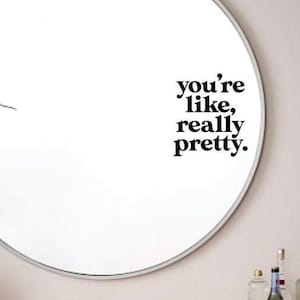 May include: A round mirror with a white frame and the text "you're like, really pretty." on the mirror surface.