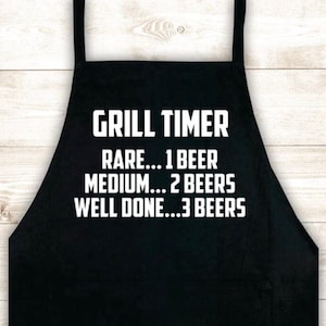 May include: Black apron with white text that reads "Grill Timer" and a list of doneness levels for meat, with corresponding beer counts: "Rare... 1 Beer", "Medium... 2 Beers", "Well Done... 3 Beers".