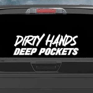 May include: White vinyl decal with the text "Dirty Hands Deep Pockets" on a black truck tailgate.