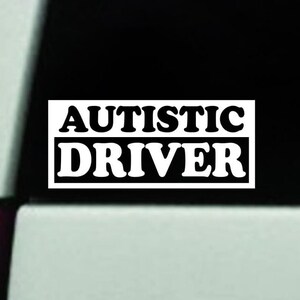 May include: White vinyl sticker with black text that reads "AUTISTIC DRIVER" on a black background.