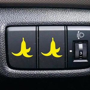 May include: Close-up of a car's interior with three buttons. The two left buttons have yellow banana peel stickers on them. The right button has a knob with the number "3" on it.