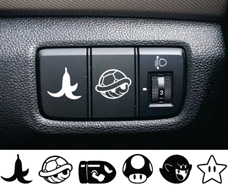 K&ouml;nnte beinhalten: Ein schwarzer Innenraum eines Autos mit einer Reihe von drei Kn&ouml;pfen. Der linke Knopf hat eine Bananenschalengrafik, der mittlere Knopf hat eine Schildkr&ouml;tenpanzergrafik und der rechte Knopf hat einen Knopf mit einem Lichtsymbol und der Zahl 3.