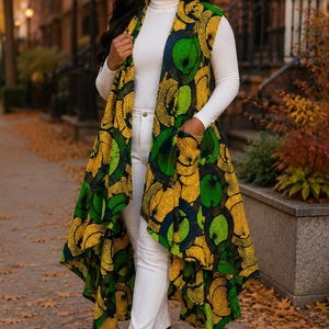 May include: A sleeveless long vest featuring a vibrant yellow, green, and dark blue circular pattern, worn over a white long-sleeve turtleneck shirt, white pants, and brown ankle boots. The vest has an open front and two front pockets.