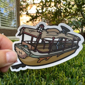 May include: A brown and green cartoon sticker of a boat with a tan awning and a red chimney. The boat has a wooden deck and a metal railing. The sticker is on a green grassy surface.
