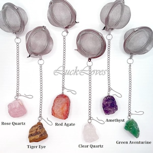 May include: Set of seven stainless steel tea infusers with chains and crystal stones. The stones are rose quartz, red agate, amethyst, tiger eye, clear quartz, and green aventurine.