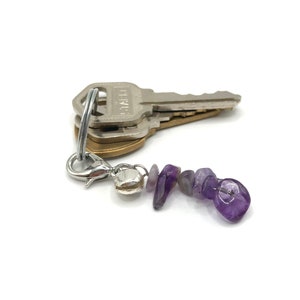 May include: A silver key chain with a set of keys and a purple amethyst stone charm.