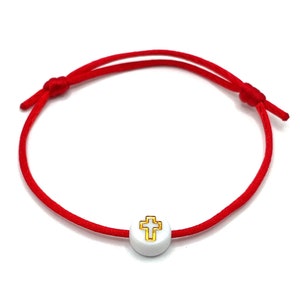 May include: Red string bracelet with a white bead featuring a gold cross.