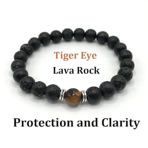 Op de afbeelding: Een zwarte lavastenen en tijgeroog kralen armband met zilveren tussenstukken. De armband ligt op een witte achtergrond en de tekst "Tiger Eye Lava Rock Protection and Clarity" staat onder de armband.