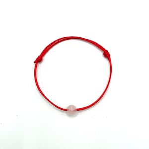 May include: A red string bracelet with a single, light pink, round bead.
