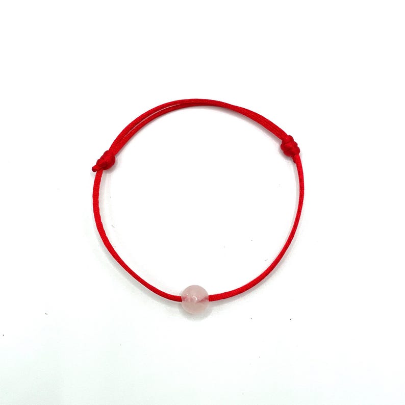 May include: A red string bracelet with a single, light pink, round bead.