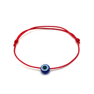 May include: A red string bracelet with a blue evil eye charm. The charm has a white centre and a black pupil.
