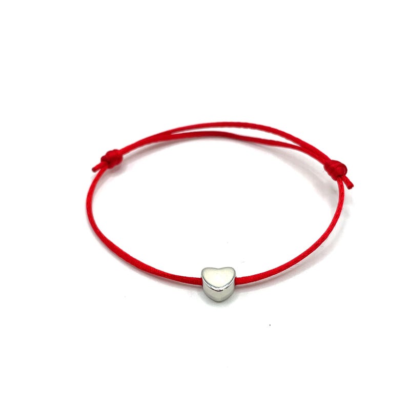 May include: A red string bracelet with a silver heart charm.